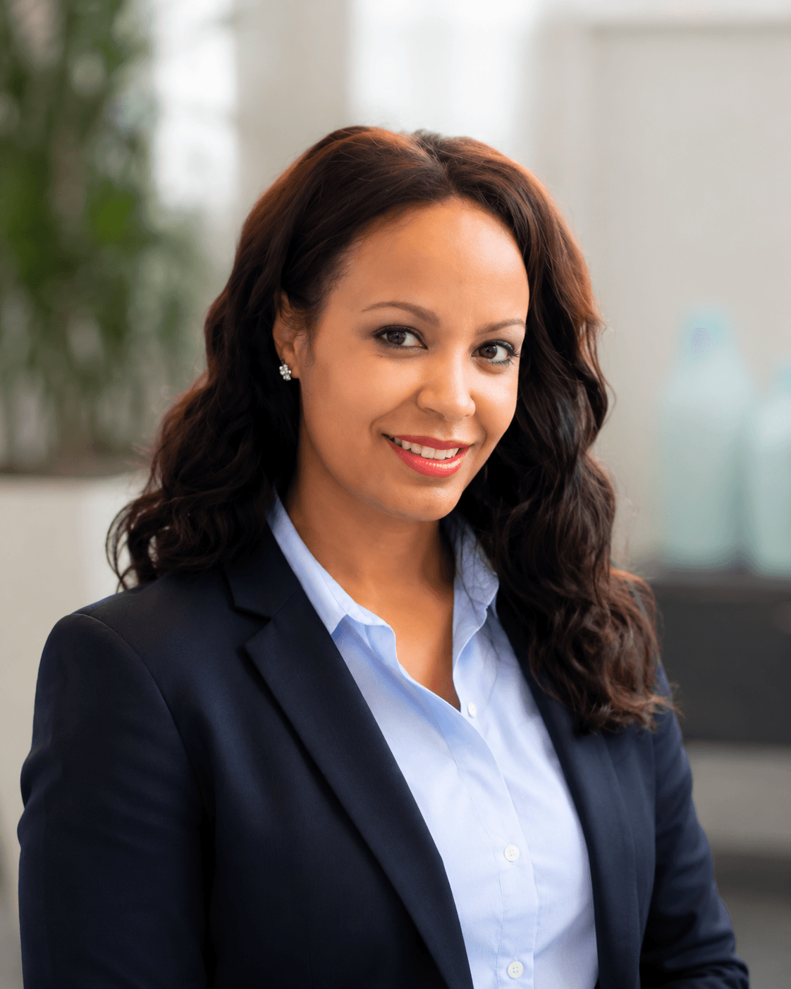 Smiling woman with long dark wavy hair wearing a navy blazer and light blue shirt.